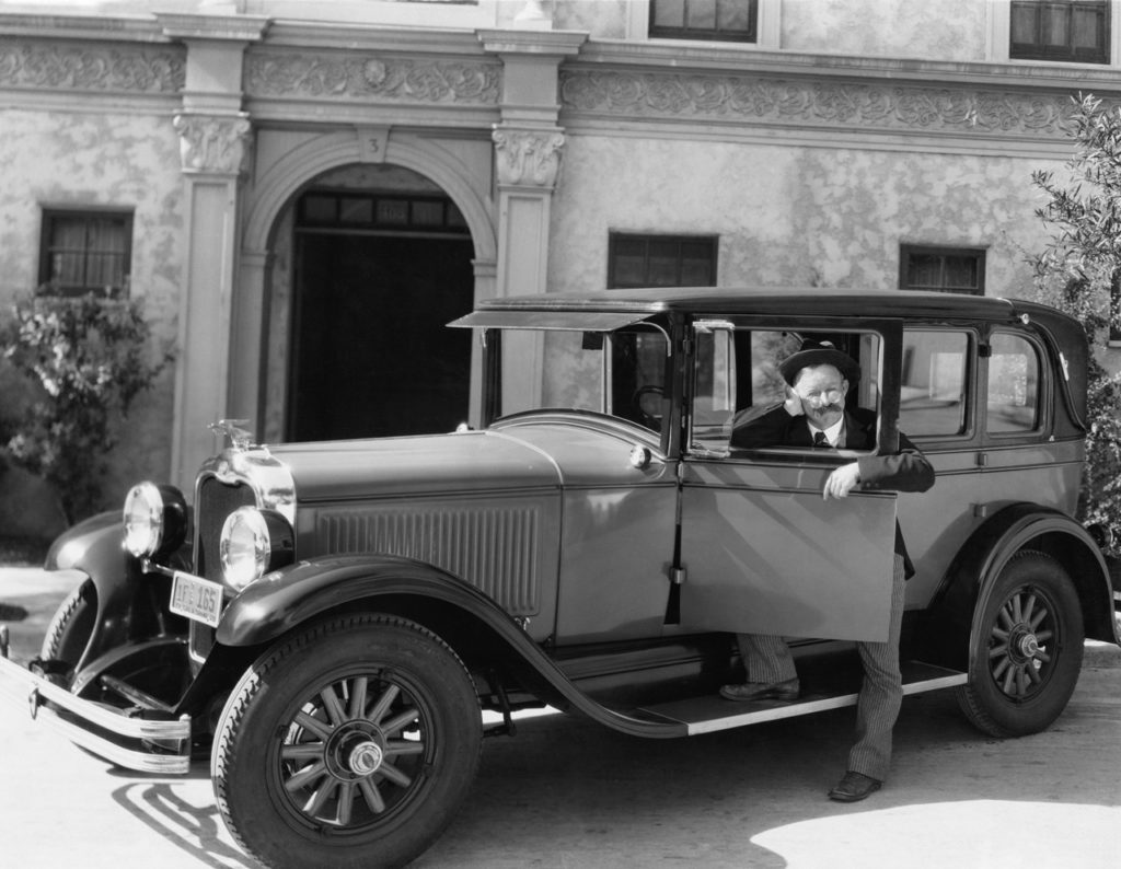 Homme posant avec sa voiture ancienne