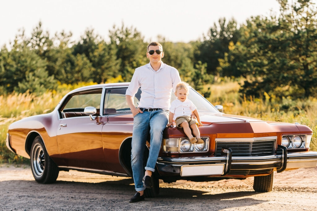 Un père et son fils assis sur le capot d'une voiture américaine de collection