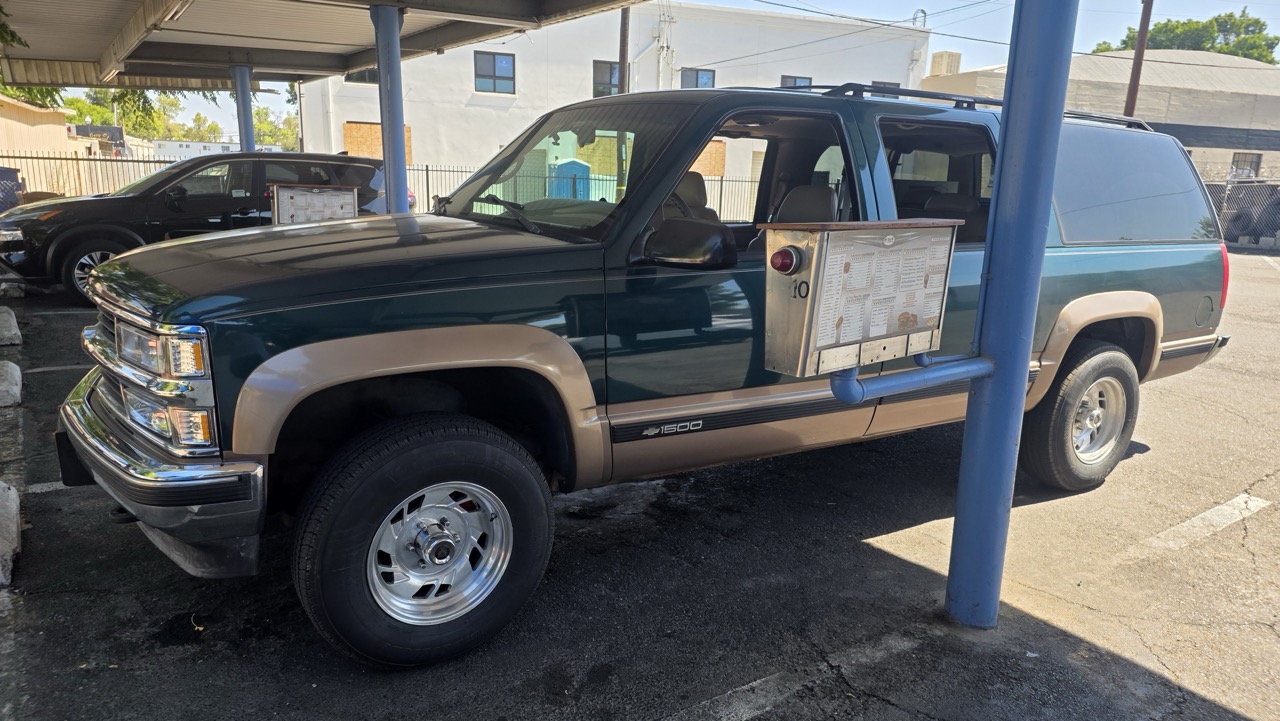 Chevrolet Suburban 1995 garé sous l'auvent d'un drive-in, plateau de carhop accroché à la vitre